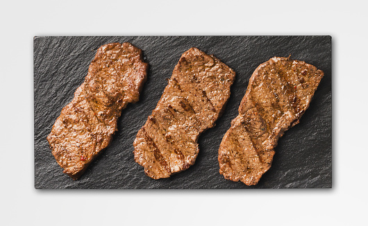 Pork steaks on black slate, isolated. Barbecue meat, top view, cutout