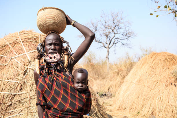 Mursi tribe woman with a child Jinka, Omo River Valley, Ethiopia - 01/10/2018 Mursi tribe lady carrying her baby and a basket on her head, decorated with traditional mursi plate in lip, corns and scars omo river photos stock pictures, royalty-free photos & images