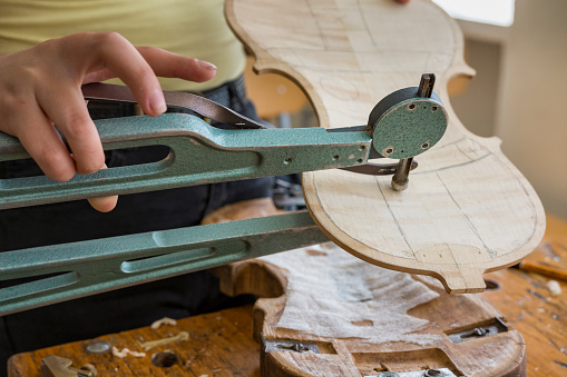 Violin maker, luthier crafting violin measuring thickness with special tool.