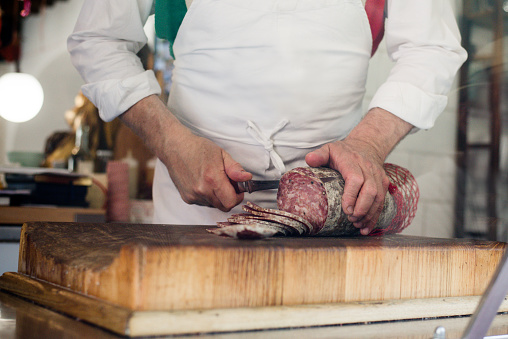 Hands of butcher cutting salami in slices