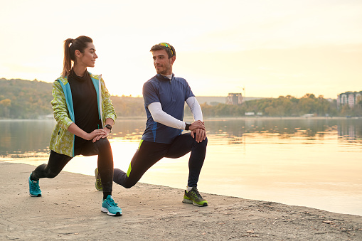 Young running couple warming up and stretching before running outdoors in the morning