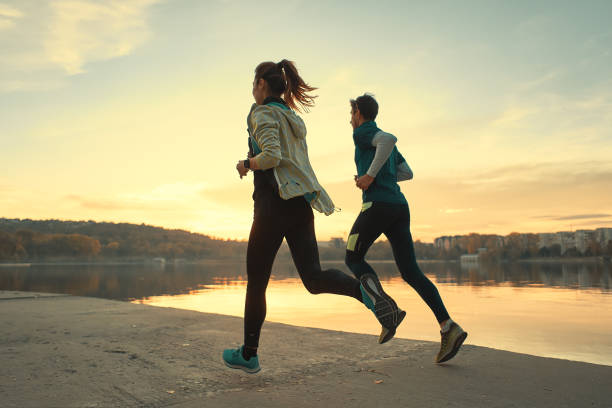Young man and woman out for a run on the lake at the sunrise stock photo