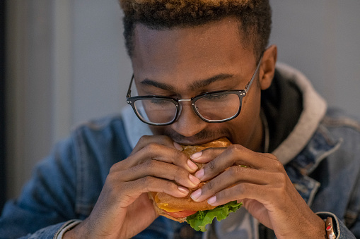 A handsome young university student of african descent enjoys his time on campus. He is eating a burger for lunch.
