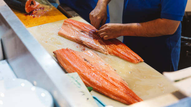 istock Chef cutting fresh salmon and remove bones from filet belly by hands for making sushi and sashimi on wooden counter. 1084615526