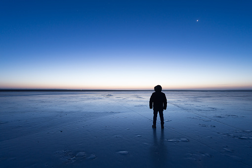 Man standing the frozen lake at dawn