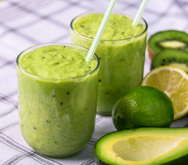 istock Green smoothie on tablecloth with avocado, lemon and kiwi on the right side. 1084636080