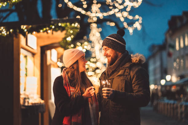 With you by my side I could never get lost! - Christmas vacations Young happy couple lighting up a sparkling stick. Women and men holding a sparkling stick at Christmas market, feeling the festive vibes, Christmas is almost here. christmas market photos stock pictures, royalty-free photos & images