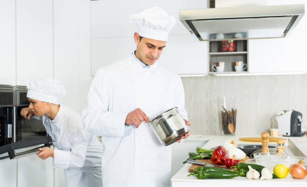 istock Professional chef  in uniform with pot  working with woman cook on kitchen 1084636468