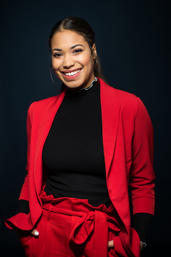 Portrait of attractive young mixed race woman standing with her hands in pocket on black background. Smiling young woman in stylish casuals.