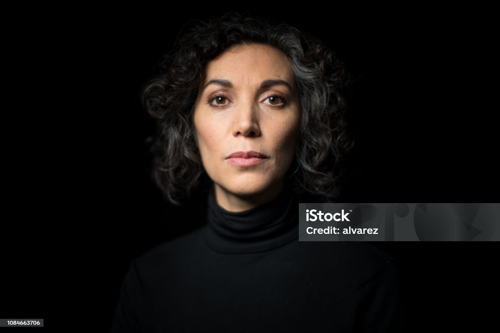 Portrait mature woman staring at camera Portrait mature woman staring at camera on black background. Close-up portrait of mature woman  having short curly hair with blank expression. Portrait Stock Photo