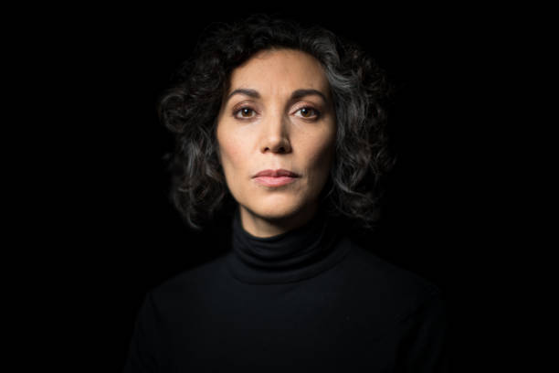 Portrait mature woman staring at camera Portrait mature woman staring at camera on black background. Close-up portrait of mature woman having short curly hair with blank expression. middle aged woman fashion stock pictures, royalty-free photos & images