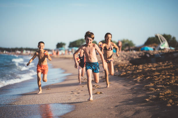 enfants en cours d’exécution et le tir avec des pistolets à eau sur la plage - spraying beaches summer sunlight photos et images de collection