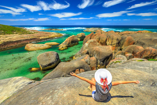 Happy woman looking the huge cracked elephant-shaped oval rocks of Elephant Rocks from promontory. Girl enjoying boulders of Great Southern Ocean in William Bay NP near Denmark, Western Australia.
