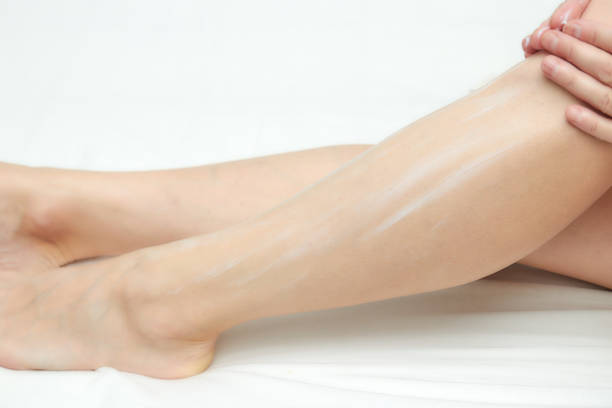 istock Woman applying moisturizer on her legs on a white background. sitting on the bed. 1084710558