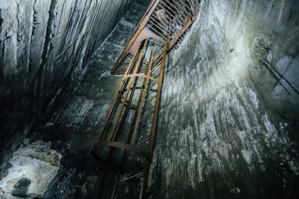 Abandoned deep vertical underground mine shaft. Old rusty iron ladder.