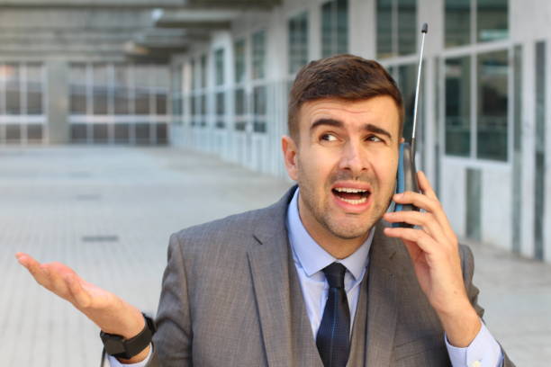 Puzzled businessman using obsolete wireless phone with antenna Puzzled businessman using obsolete wireless phone with antenna. misspelled stock pictures, royalty-free photos & images