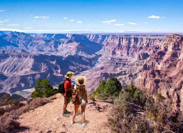 Couple on top of the mountain, looking at beautiful summer mountain  landscape. Friends on hiking trip enjoying view of Colorado river. South Rim. Grand Canyon National Park, Arizona, USA.