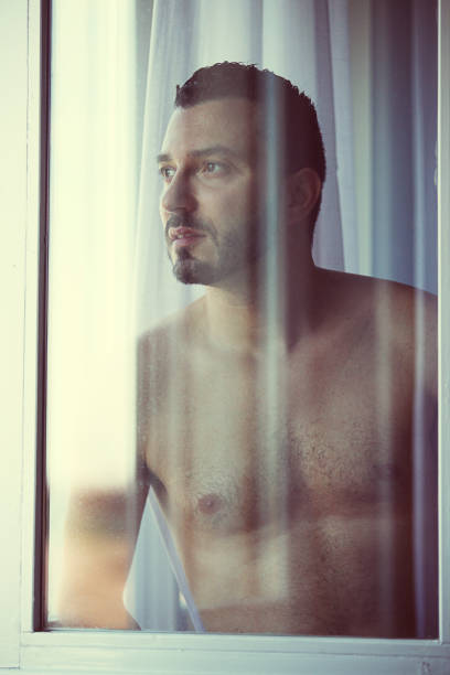 istock Sexy man looking through the window 1084733632