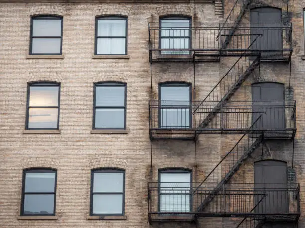 Photo of Fire escape stairs and ladder, in metal, on a typical North American old brick building from the Old Montreal, Quebec, Canada. These stairs, made for emergency, are symbolic of the architecture