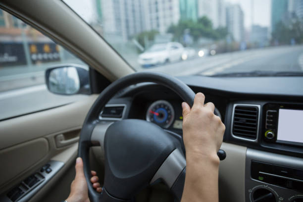 istock Hands holding steering wheel while driving car on city road 1084756188