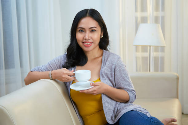Woman drinking tea Pretty cheerful young Asian woman enjoying cup of tea at home hot filipina women stock pictures, royalty-free photos & images