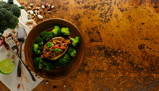 Healthy super food vegetarian chili made with a variety of beans and pulses served on a baked potato with freshly steamed broccoli, sprinkled with lime juice, set on a terracotta background. Shot directly above, good copy space, shallow depth of field.