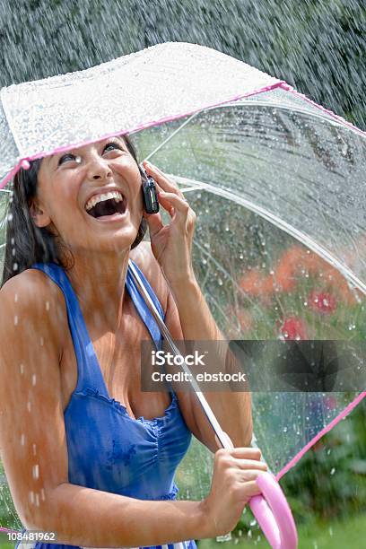 Giovane Donna Utilizzando Un Cellulare E Ombrelloni In Pioggia - Fotografie stock e altre immagini di Acqua