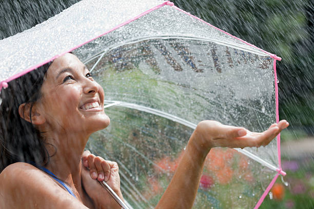 Smiling young woman using umbrella in rain stock photo
