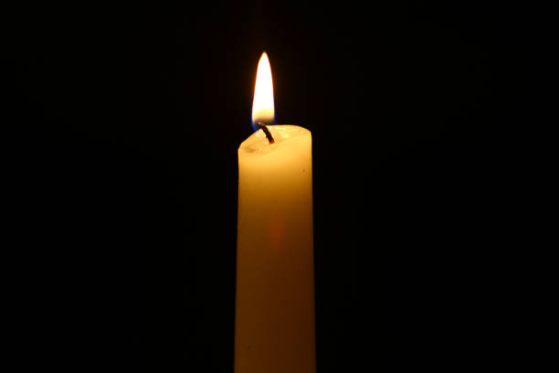 istock tiny wax glowing yellow candle with vivid fire against the heavy black background. 1084823786
