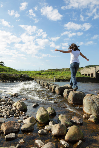 Young girl runs across stepping stones  to cross a stream