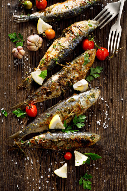 peixe frito com adição de ervas, especiarias e fatias de limão em um fundo de madeira. - gastronomia de portugal - fotografias e filmes do acervo