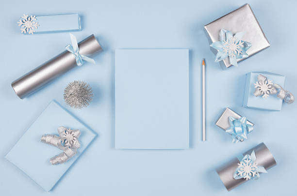 istock Christmas background for your design and text - blank paper and silver pencil, soft pastel blue and gift boxes with bows, christmas tree on blue backdrop, top view, copy space. 1084843376