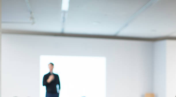istock Presenter Presenting Presentation to Conference Audience. De-focused Blurred . Lecturer on Stage at Tech Forum. Speaker Giving Speech in Conference Hall Auditorium. Copy Space Screen Background. 1084848550