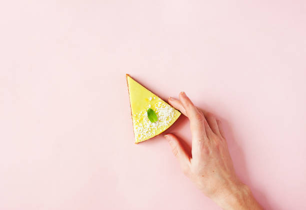 здоровый десерт - сырой веганский лимонный и кокосовый торт на розовом фоне с женской рукой - современная летняя еда минимальная концепция,  - healthy eating close up lemon nut стоковые фото и изображения