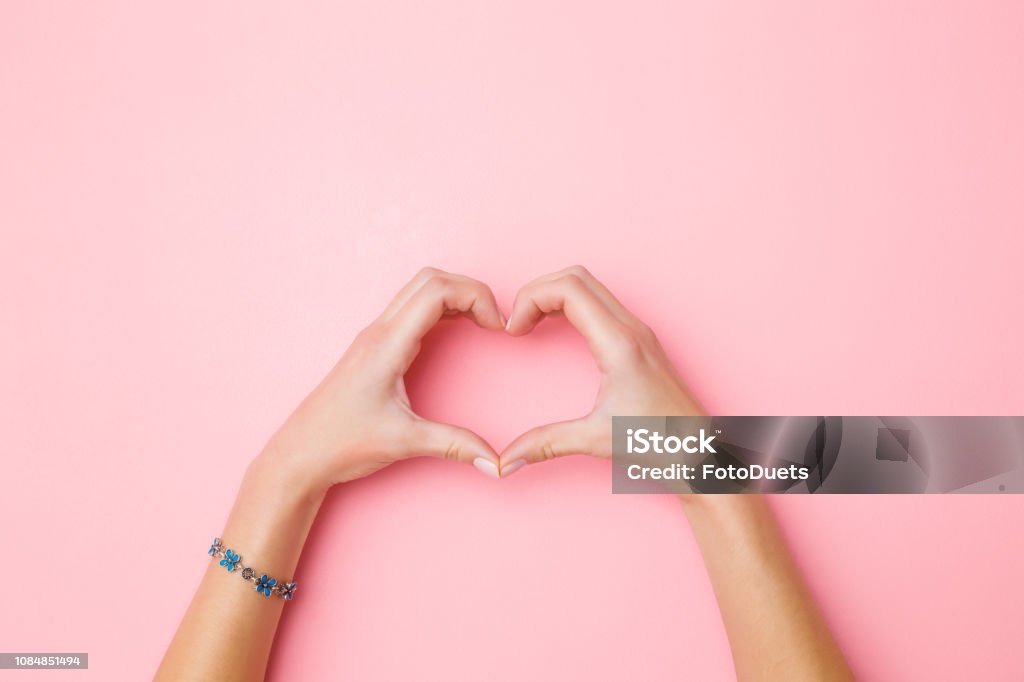Heart shape created from young woman's hands on pastel pink background. Love and happiness concept. Empty place for emotional, sentimental text, quote or sayings. Closeup. Top view. Hand Stock Photo