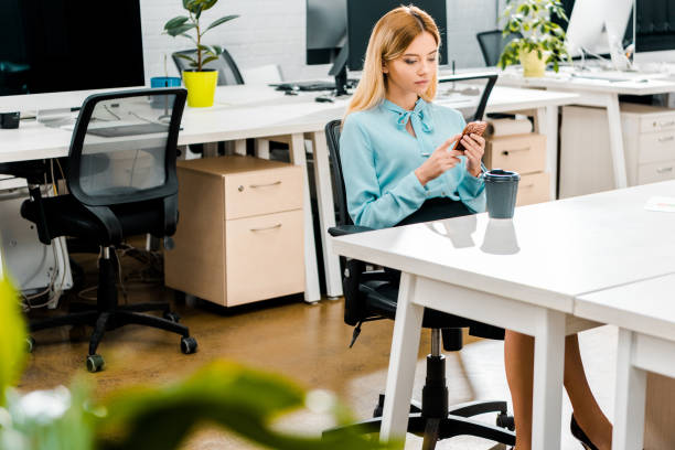 istock young businesswoman using smartphone at workplace with coffee to go 1084853406