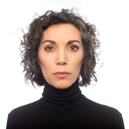 Close-up portrait of mature woman with short curly hair staring at camera. Mid adult female with blank expression on white background.
