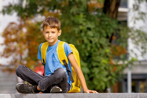 Cute smart boy with backpack sitting outdoors after school
