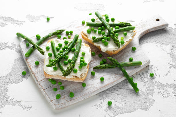 istock Appetizer bruschetta, toast with Asparagus, Peas and creamy soft cheese. on white board. 1084866372