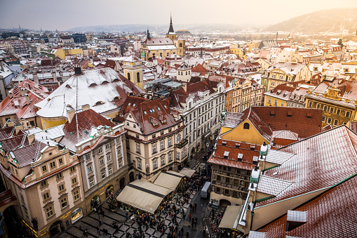 Color image depicting a high angle view of the rooftops and old architecture of Prague old town in Czech Republic. In the town square below people and tourists are browing the many stalls of the Christmas market. Image shot on a cold winter's day. Room for copy space.
