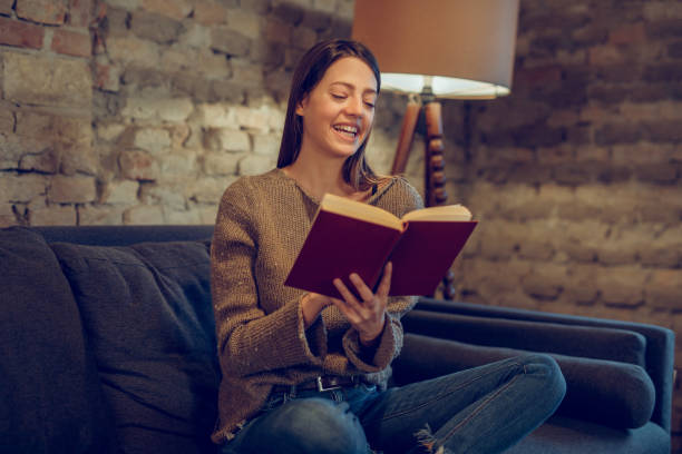 istock Young woman sitting on sofa reading a book 1084878244