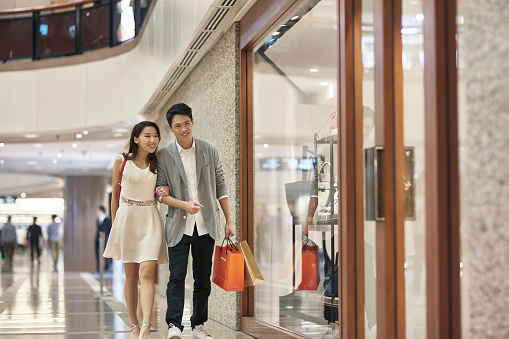 Full length of young couple window shopping in luxury mall. Male and female lovers admiring purse in store window. They are enjoying weekend together.
