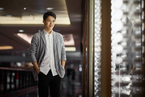 Handsome young man window shopping in luxury mall. Happy male is standing with hands in pockets. He is wearing cardigan sweater.