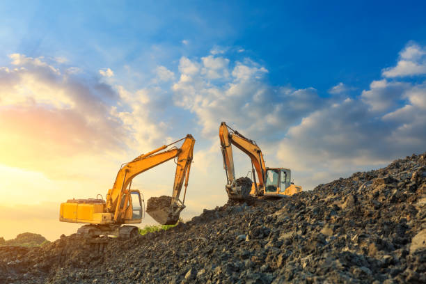 due escavatori lavorano in cantiere al tramonto - earth mover working field dirt foto e immagini stock