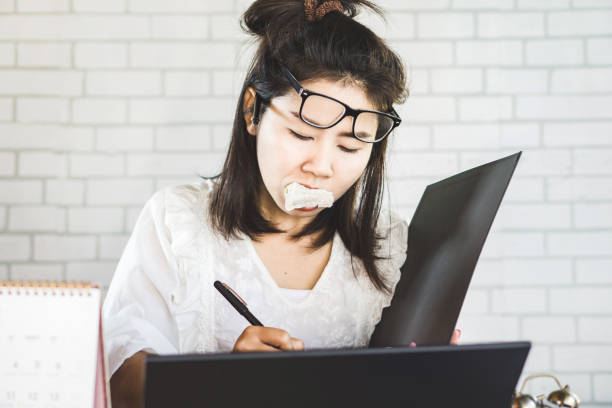 workaholic asiatin beschäftigt mit arbeiten und essen sandwich in der gleichen zeit am schreibtisch - eating sandwich emotional stress food stock-fotos und bilder