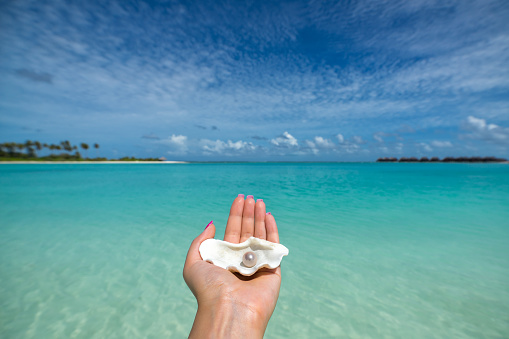 Open shell with a pearl on tropical beach in the woman's hand