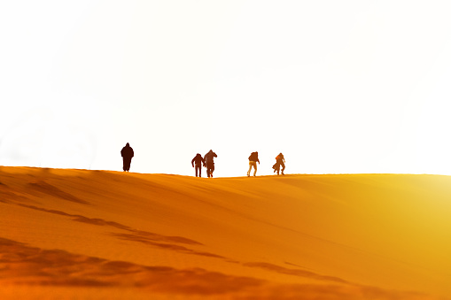 People walking over yellow sand dune hill at sunset