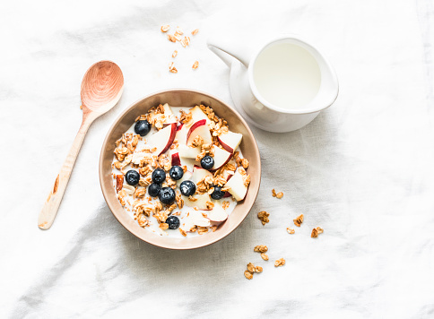 Peanut butter granola with milk, apples and blueberries - healthy energy breakfast or snack on a light background, top view. Copy space