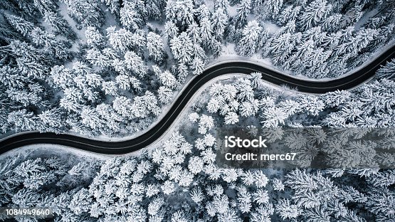 istock Curvy windy road in snow covered forest, top down aerial view 1084949640