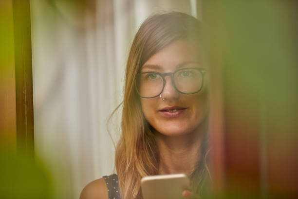 istock Young woman using smart phone indoors. Window reflection from outdoors. 1084962878